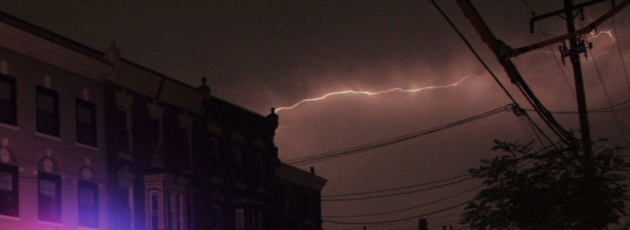 lightning in the clouds behind a house and powerlines