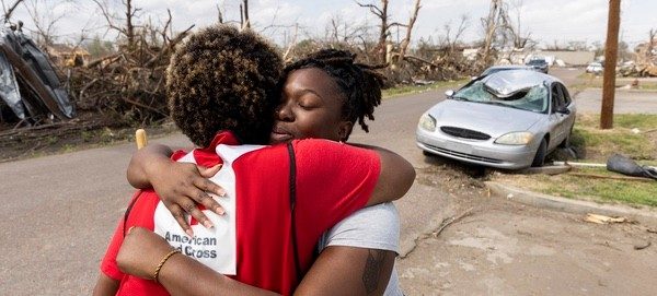 a woman hugs a Red Crosser wearing their red vest near their home after a disaster