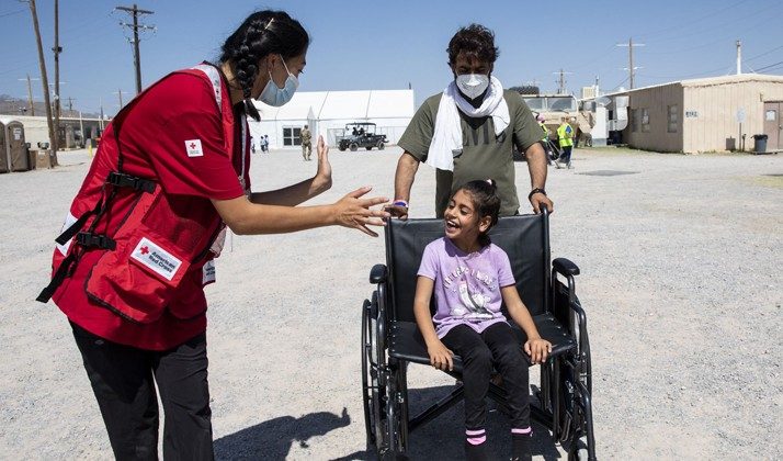 A Red Cross Volunteer is helping a student provide assistance to a young girl in a wheelchair