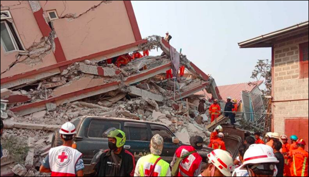 Responders in Red Cross hard hats and vests in front of destroyed structure